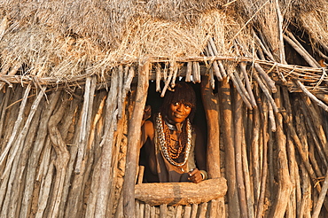 Pregnant Hamar woman with necklaces made of cowry shells coming out of her wooden hut, Omo River Valley, Southern Ethiopia, Africa