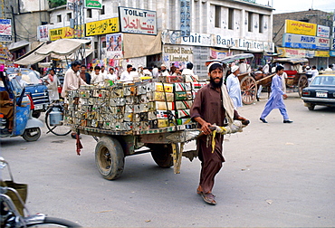 A man in Islamabad, Pakistan dragging a trailer loaded with empty oil cans through the crowded street.