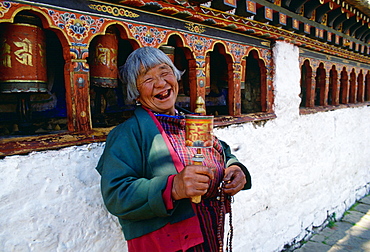 An old woman with prayer wheels laughing at the Kyichu Buddhist Temple in Paro, Bhutan