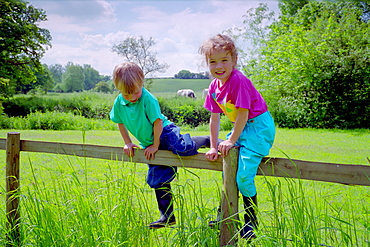 A four year old boy and six year old girl climbing a wooden fence in Wiltshire, England