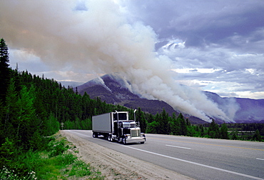 Articulated truck driving past the smoke of a forest fire in Canada