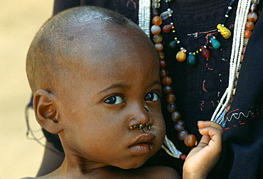 With flies around his nose a child holds onto his mother's necklace at Gorom Gorom Hospital in Burkina Faso