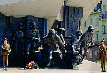 Soldiers standing at attention and holding rifles as they guard the Warsaw Uprising Monument in Poland.