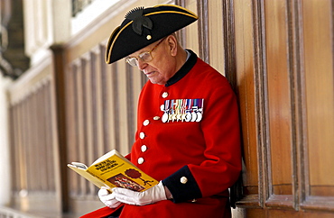 Chelsea Pensioner Alan Gale at the Royal Hospital Chelsea in uniform with his military medals reading a book on wood carving