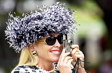 Race-goer wearing a typical Ascot fashion hat while photographing the day's events on a small camera at Royal Ascot Races