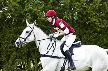 Young man rides a grey mare horse in an eventing competition, United Kingdom