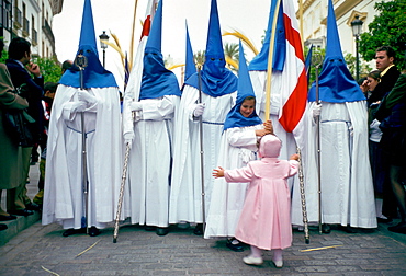 Procession for 'Semana Santa', Holy Week in Seville, Spain (Sevilla) - a young girl with open arms reaches out to hug a hooded girl in the parade.