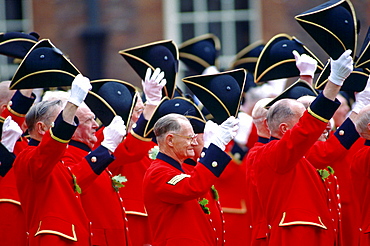 Chelsea Pensioners, dressed in their traditional uniform of bright red jacket, raising their tricorn hats and cheering during the Founder's Day Parade outside the Royal Hospital in Chelsea.