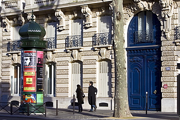 Couple walk past obelisk advertising theatre productions in Parisian street, Boulevard St Germain, Latin Quarter, France