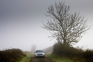 BMW 5-series car drives along empty country road in adverse foggy weather, Oxfordshire,  England, United Kingdom