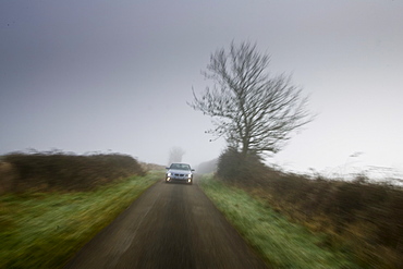 BMW 5-series car drives along empty country road in adverse foggy weather, Oxfordshire,  England, United Kingdom