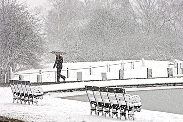 Man walks with umbrella across snow-covered Hampstead Heath, North London, United Kingdom