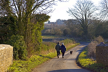 Couple walk their dog on a country lane in Asthall Leigh, Oxfordshire, United Kingdom