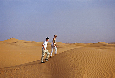 Young man and woman walk up sand dunes in the Sahara Desert, Morocco