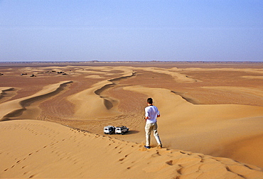 Young man walks down the sand dunes in the Sahara Desert, Morocco