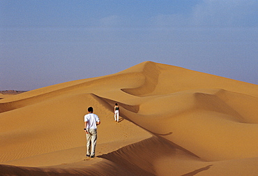 Tourists climbing a sand dune in the Sahara Desert, Morocco.