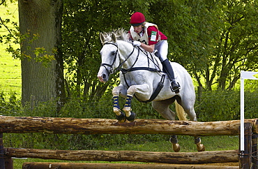 Young man rides a grey mare horse in an eventing competition, United Kingdom