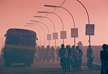 Early morning rush hour in the streets of Delhi, India.  Commuters on bicycles are overtaken by the bus.