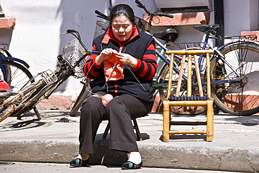 Woman sits knitting in Zi Zhong Road, old French Concession Quarter in Shanghai, China