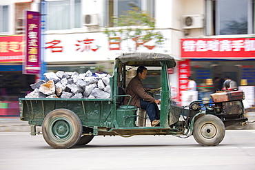 Man drives delivery tractor containing pile of construction stones in Yangshuo street, China