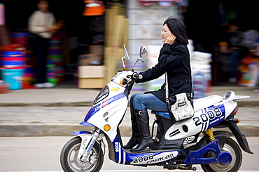 Woman on a scooter using mobile phone in Yangshuo street, China