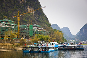 Tourist boats moored on the Li River at Yangshuo by a hotel construction site, China