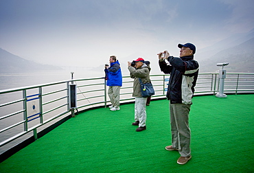 Tourists take photographs from the deck of a Victoria Line Cruise Ship, Yangze River, China