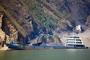 Freight ship being loaded with coal from delivery trucks on the shore, in Three Gorges area, Yangtze River, China