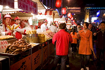 Shoppers pass stalls selling meat kebabs and corn on the cobs in the Night Market, Wangfujing Street, Beijing, China