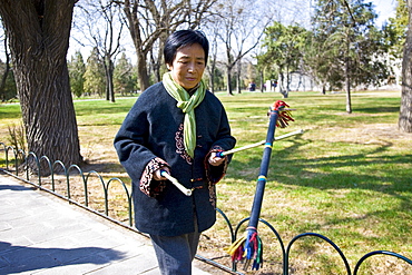 Woman practises tai chi with sticks in park of the Temple of Heaven, Beijing, China