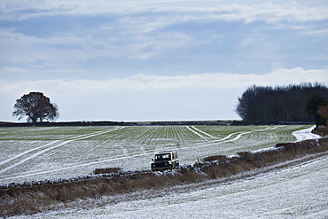 Land Rover driving along frosty track in wintry landscape in The Cotswolds, Oxfordshire, UK