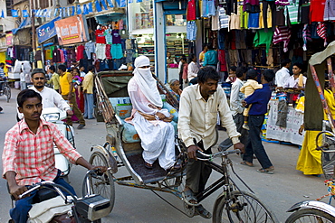 Street scene in holy city of Varanasi, young muslim woman in white burkha rides in rickshaw, Benares, Northern India