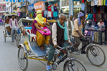 Street scene in holy city of Varanasi, young muslim woman in coloured burkha rides in rickshaw, Benares, Northern India