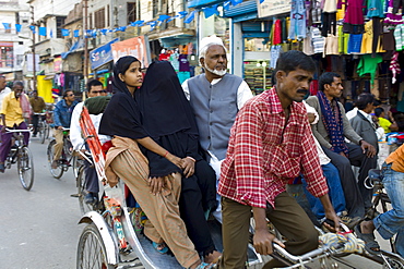 Street scene in holy city of Varanasi, muslim family ride in rickshaw, Benares, Northern India