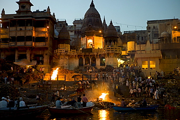 Tourists watch body bathed in River Ganges and traditional Hindu cremation on funeral pyre at Manikarnika Ghat in Holy City of Varanasi, Benares, India