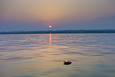 Ceremonial lit candle carries Hindu prayers on River Ganges at sunrise by holy city of Varanasi, Benares, Northern India