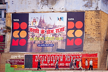 Indian people walking past TATA Docomo posters by the Ganges in holy city of Varanasi, Benares, Northern India