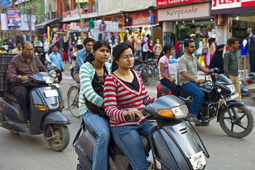 Young Indian girls ride motor scooter in street scene in city of Varanasi, Benares, Northern India