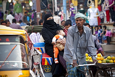 Muslim woman and child travel by rickshaw in crowded street scene in city of Varanasi, Benares, Northern India