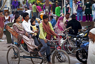 Young Indian family travel by rickshaw in crowded street scene in city of Varanasi, Benares, Northern India