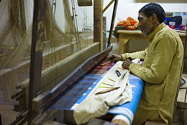 Indian man working loom at silk factory making textiles and saris at Bressler near Varanasi, Benares, Northern India