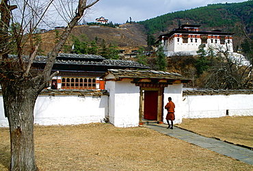 A man walking through the grounds of the Ugyen Pelri Palace in Bhutan.  The Paro Dzong can be seen on the hill behind.