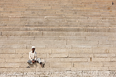 Hindu man sits on steps of Chet Singh Ghat on banks of The Ganges River in holy city of Varanasi, India