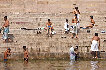 Indian Hindu pilgrims men and boys bathing in The Ganges River by steps of the Ghats in Holy City of Varanasi, Benares, India