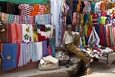 Stallholder selling clothes and sari fabrics and other textiles at Varanasi, Northern India