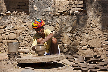 Indian potter in traditional Rajasthani turban works on potter's wheel at home making clay pots in Nimaj village, Rajasthan, Northern India