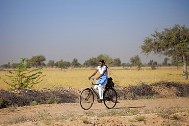 Young Indian girl in school uniform riding bicycle to her school near Rohet in Rajasthan, Northern India