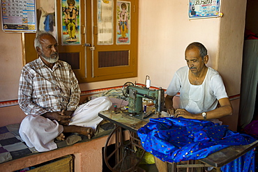 Indian man with traditional sewing machine making sari in Rajasthani colourful silk fabric in Narlai village in Rajasthan, Northern India