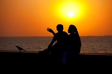 Young Indian couple sit on seawall at sunset at Nariman Point, Mumbai, formerly Bombay, India