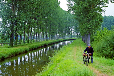 A man walking beside a canal with his bicycle in France